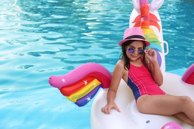 Happy cute girl on inflatable unicorn in swimming pool