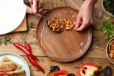 Woman making tasty spring roll at wooden table, top view