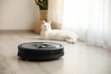 Photo of Modern robotic vacuum cleaner in room and cute white cat on background