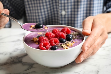 Woman eating tasty acai smoothie with fruits at white marble table, closeup