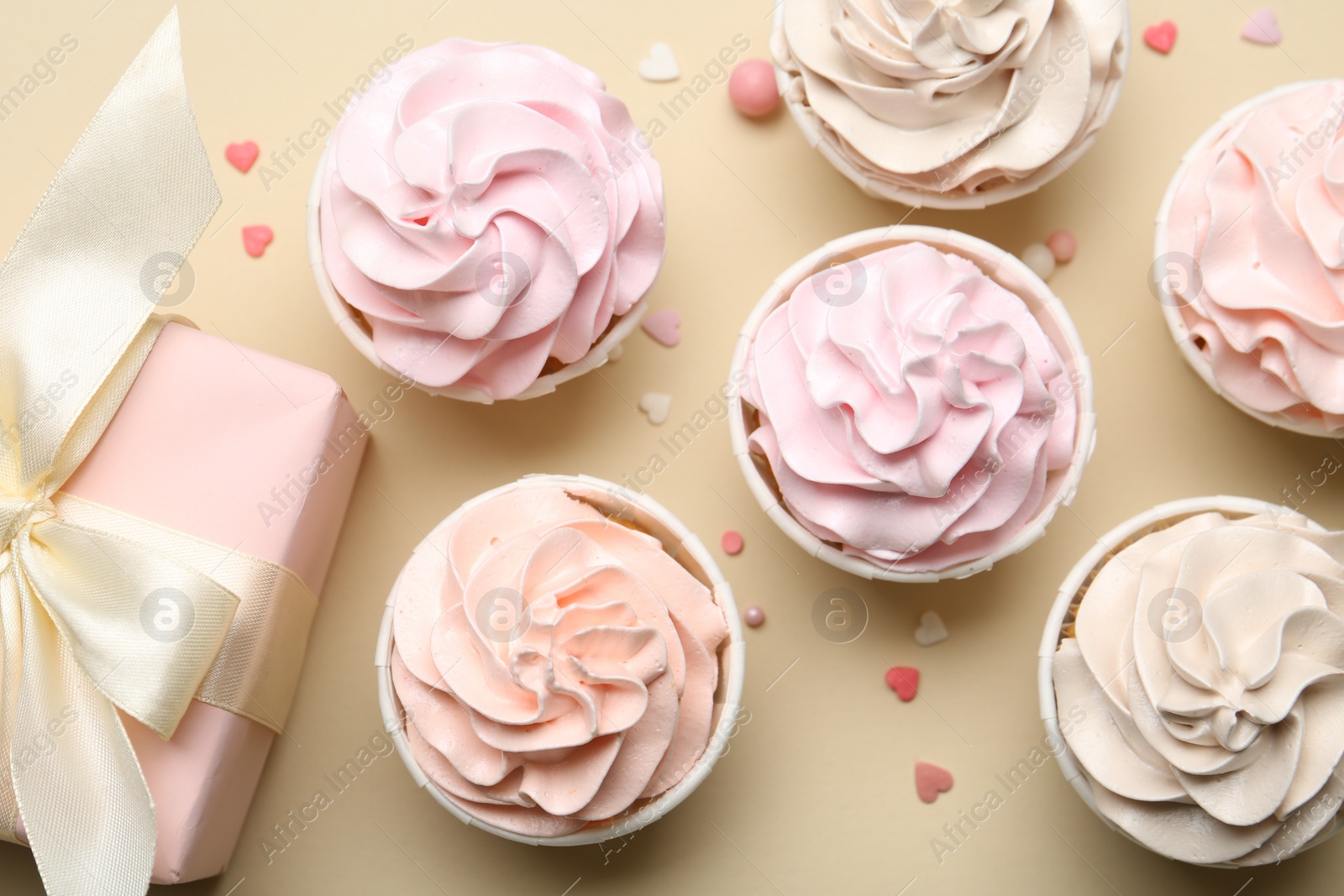 Photo of Delicious birthday cupcakes, gift box and sprinkles on beige background, flat lay