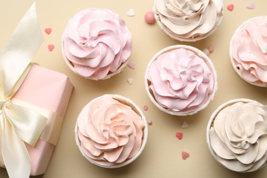 Photo of Delicious birthday cupcakes, gift box and sprinkles on beige background, flat lay