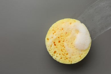 Yellow sponge with foam on grey background, top view. Space for text