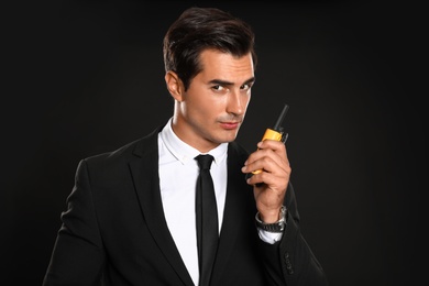 Male security guard in uniform using portable radio transmitter on dark background