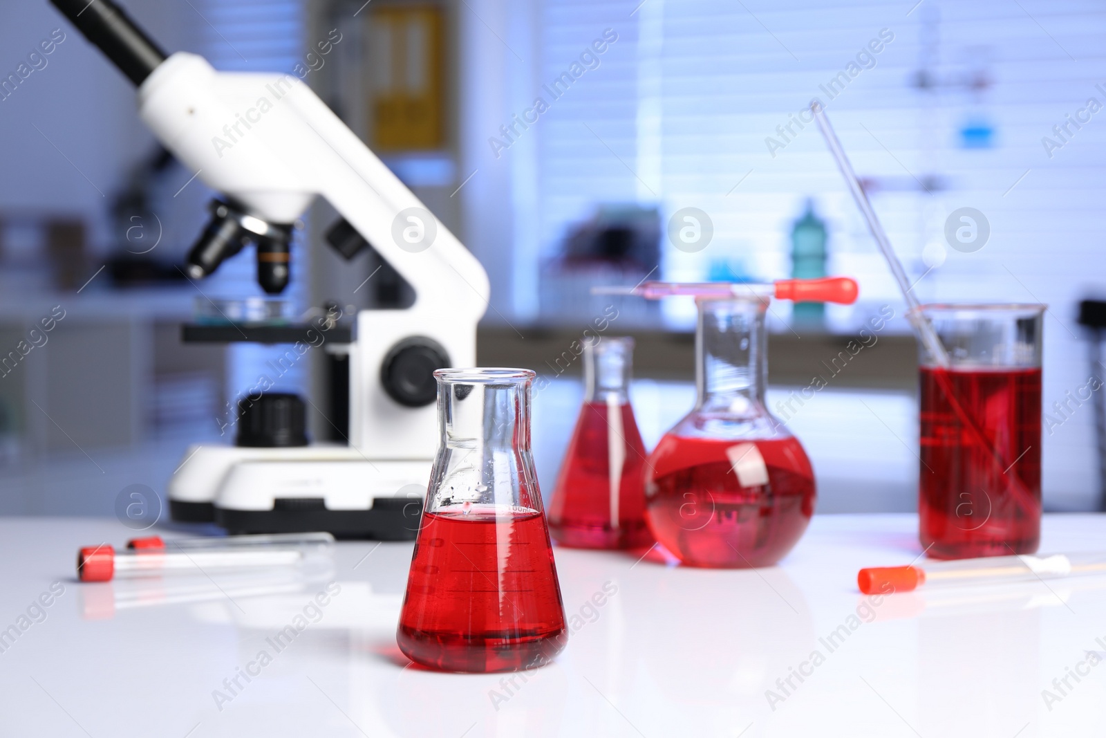 Photo of Laboratory analysis. Glass flasks with red liquid and microscope on white table indoors