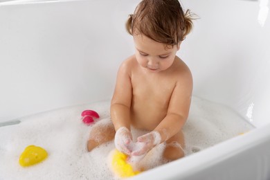 Photo of Cute little girl taking bubble bath with toys indoors