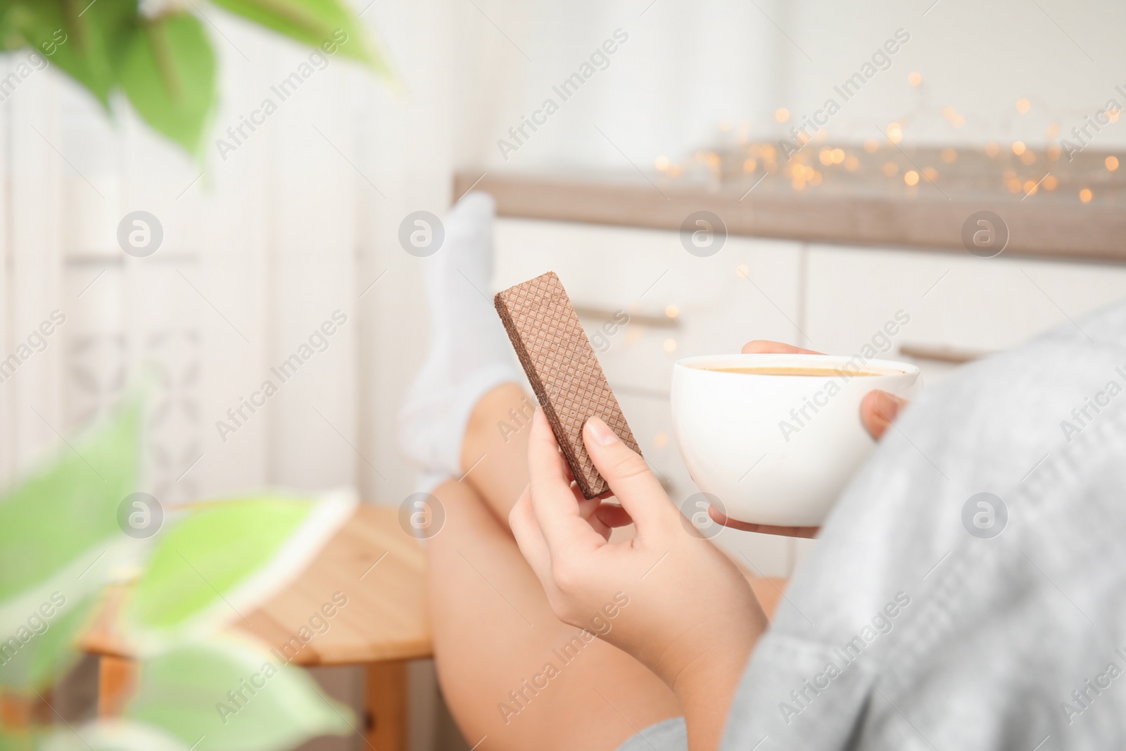 Photo of Woman having delicious wafer and coffee for breakfast indoors, closeup