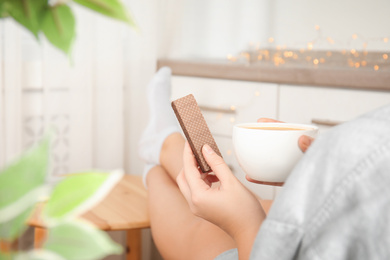 Woman having delicious wafer and coffee for breakfast indoors, closeup