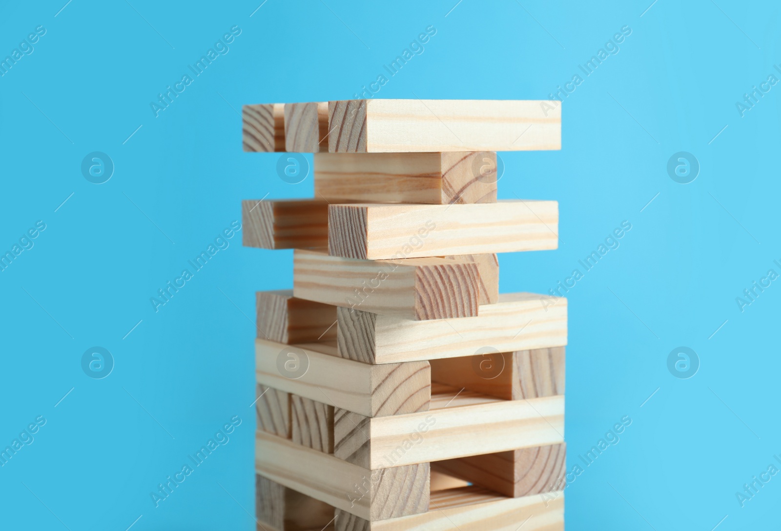 Photo of Jenga tower made of wooden blocks on light blue background, closeup