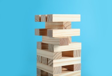 Photo of Jenga tower made of wooden blocks on light blue background, closeup