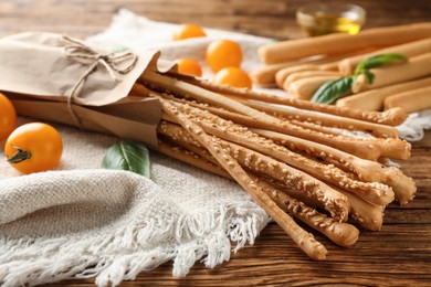 Delicious grissini sticks, basil leaves and yellow tomatoes on wooden table, closeup