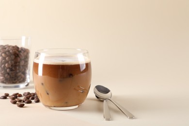 Photo of Refreshing iced coffee with milk in glass, beans and spoons on beige background, space for text