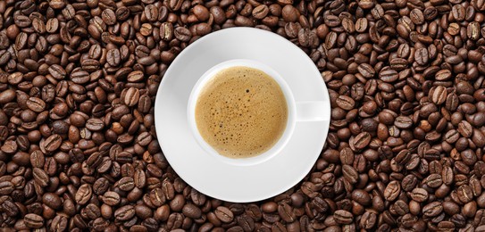 Image of Cup of tasty aromatic coffee on roasted beans, top view. Banner design