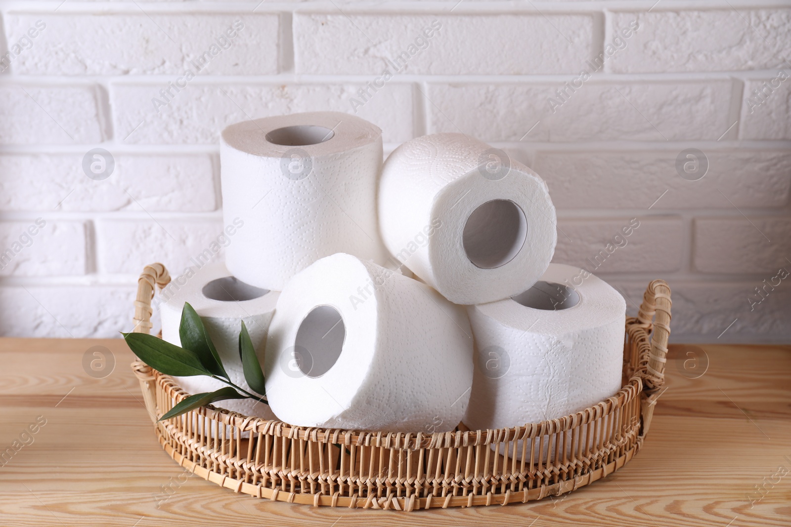 Photo of Toilet paper rolls and green leaves on wooden table near white brick wall