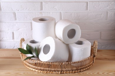 Toilet paper rolls and green leaves on wooden table near white brick wall