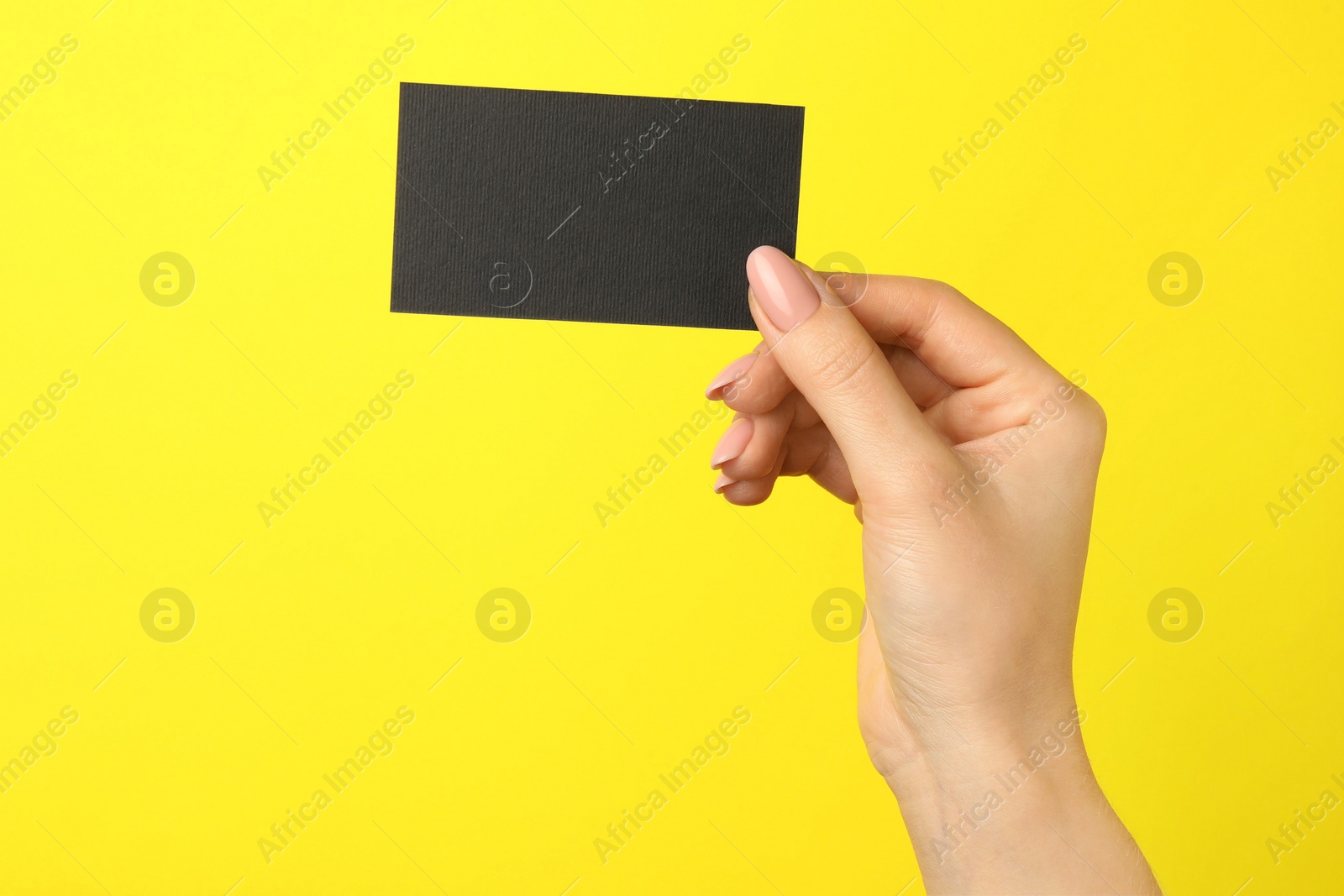 Photo of Woman with blank black business card on yellow background, closeup. Mockup for design