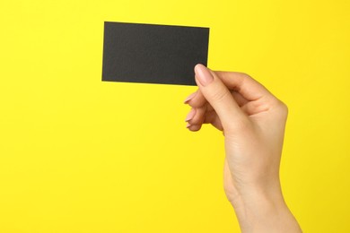 Woman with blank black business card on yellow background, closeup. Mockup for design