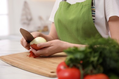 Photo of Woman peeling onion at table in kitchen, closeup. Preparing vegetable