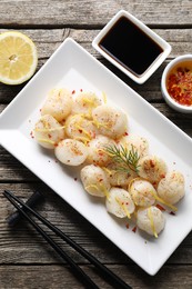 Photo of Raw scallops with spices, dill, lemon zest and sauces on wooden table, flat lay