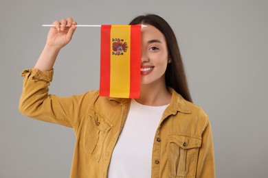 Young woman holding flag of Spain on light grey background