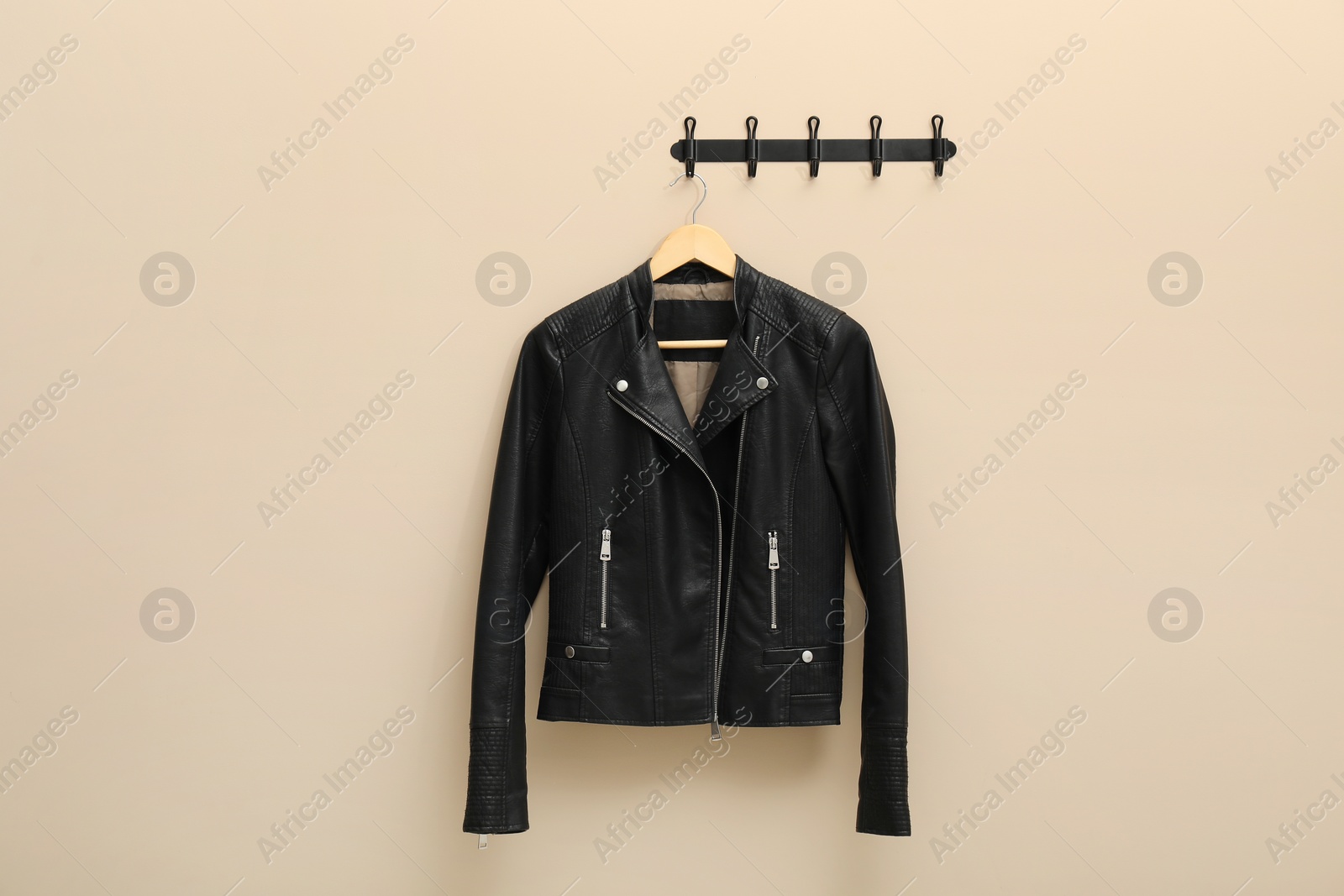 Photo of Hanger with black leather jacket on beige wall