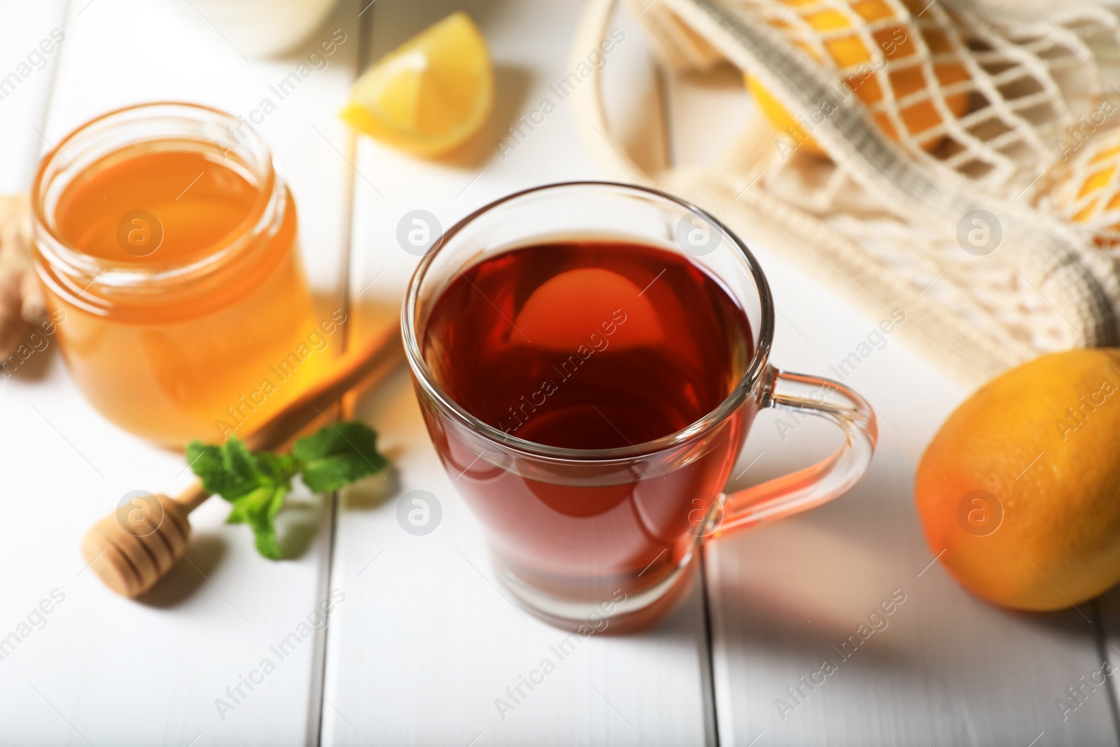 Photo of Cup of delicious ginger tea and ingredients on white wooden table, closeup