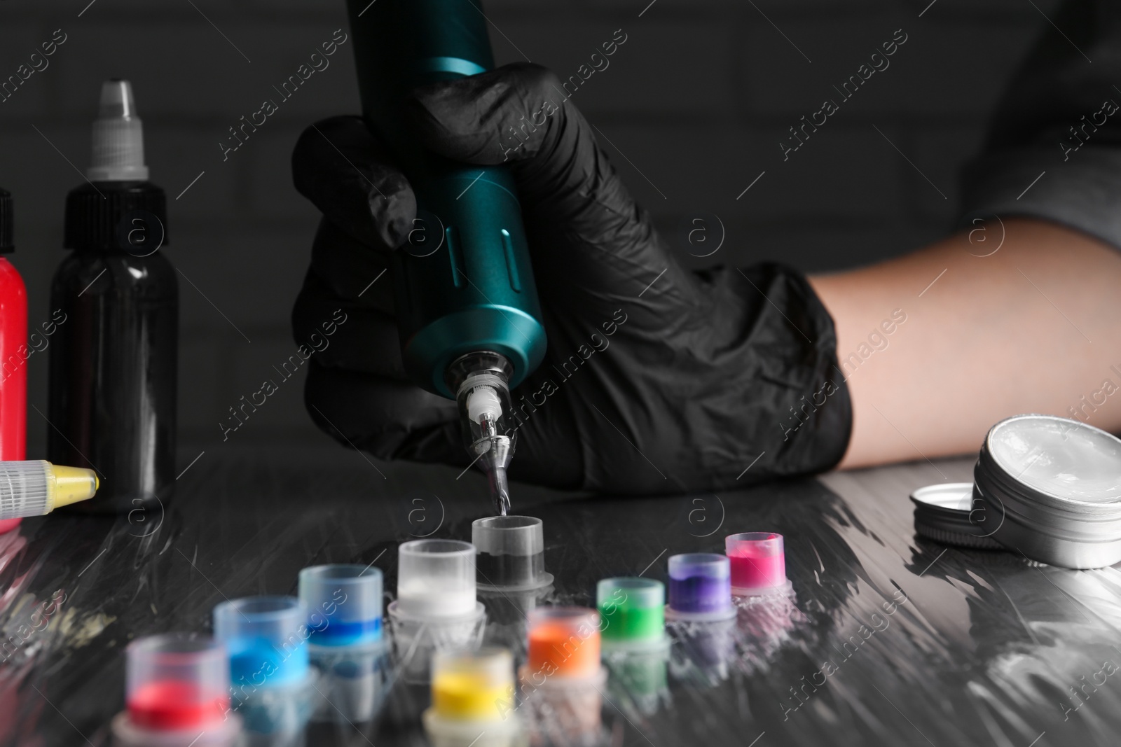 Photo of Tattoo artist with professional machine and colorful inks at table, closeup