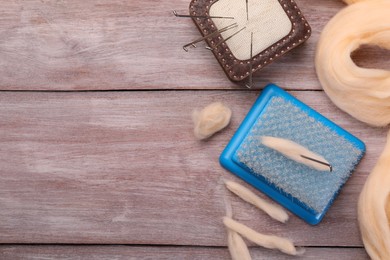 Photo of Felting tools and wool on wooden table, flat lay. Space for text