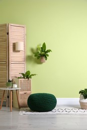 Photo of Stylish room interior with comfortable knitted pouf and plants near light green wall