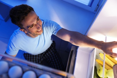 Man taking products out of refrigerator in kitchen at night, high angle view