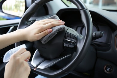 Woman cleaning steering wheel with rag in car, closeup