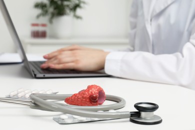 Photo of Endocrinologist working at table, focus on stethoscope and model of thyroid gland