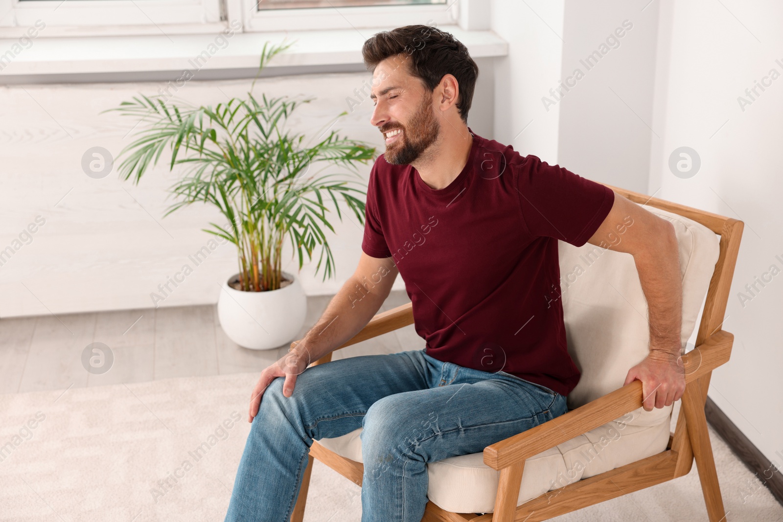 Photo of Man suffering from leg pain and touching knee on soft armchair at home