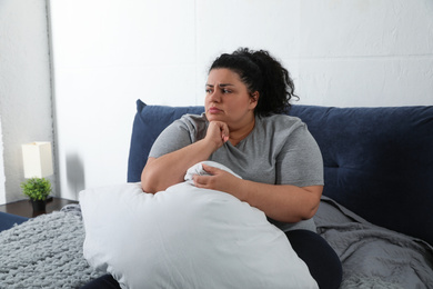 Depressed overweight woman with pillow on bed