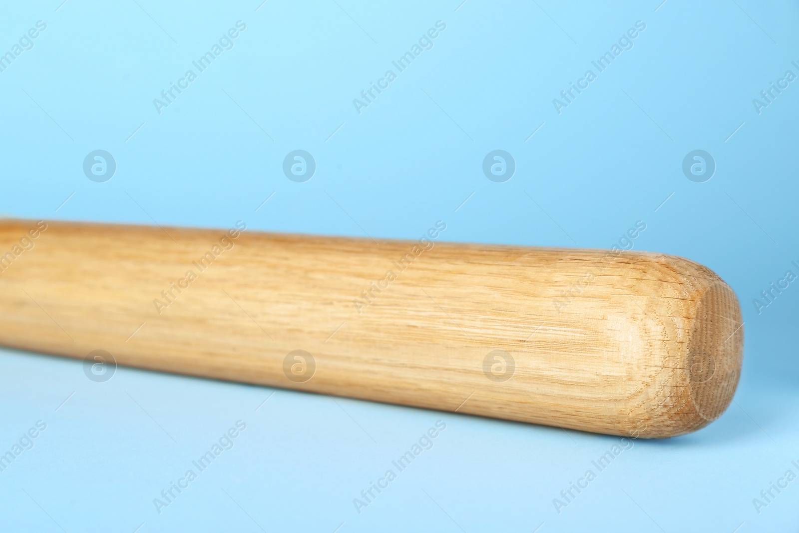 Photo of Wooden baseball bat on light blue background, closeup. Sports equipment