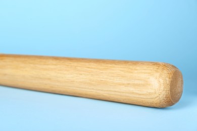 Photo of Wooden baseball bat on light blue background, closeup. Sports equipment