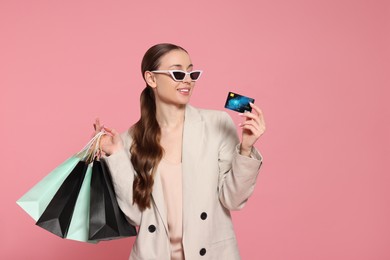 Photo of Stylish young woman with shopping bags and credit card on pink background