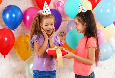 Photo of Little girl giving her friend birthday gift at party indoors