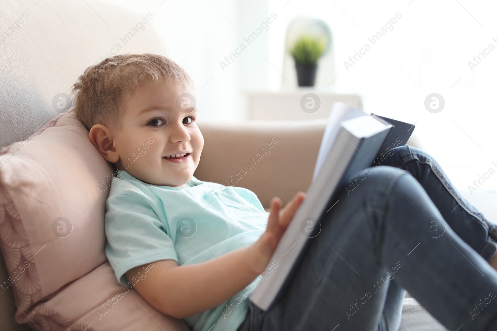 Photo of Cute child reading book on sofa indoors