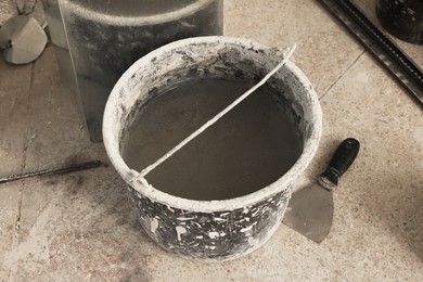 Photo of Bucket of adhesive mix and spatula on floor indoors Tiles installation process