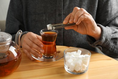 Photo of Woman adding sugar cube into aromatic tea at wooden table, closeup