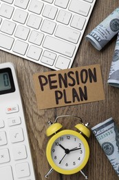 Card with words Pension Plan, banknotes, calculator and alarm clock on wooden office table, flat lay