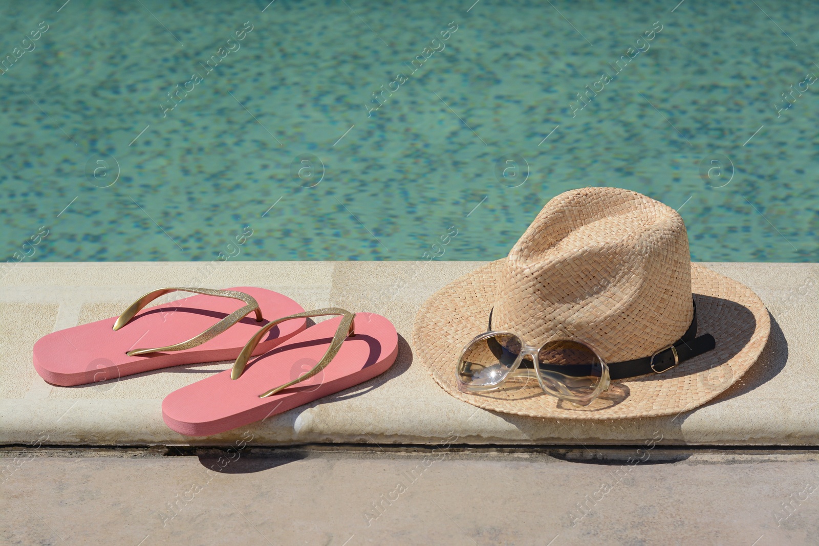 Photo of Stylish hat, flip flops and sunglasses near outdoor swimming pool on sunny day. Beach accessories