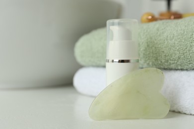 Photo of Jade gua sha tool, cosmetic product and towels on white countertop, closeup. Space for text