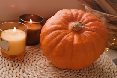 Photo of Scented candles and pumpkin on wicker mat indoors