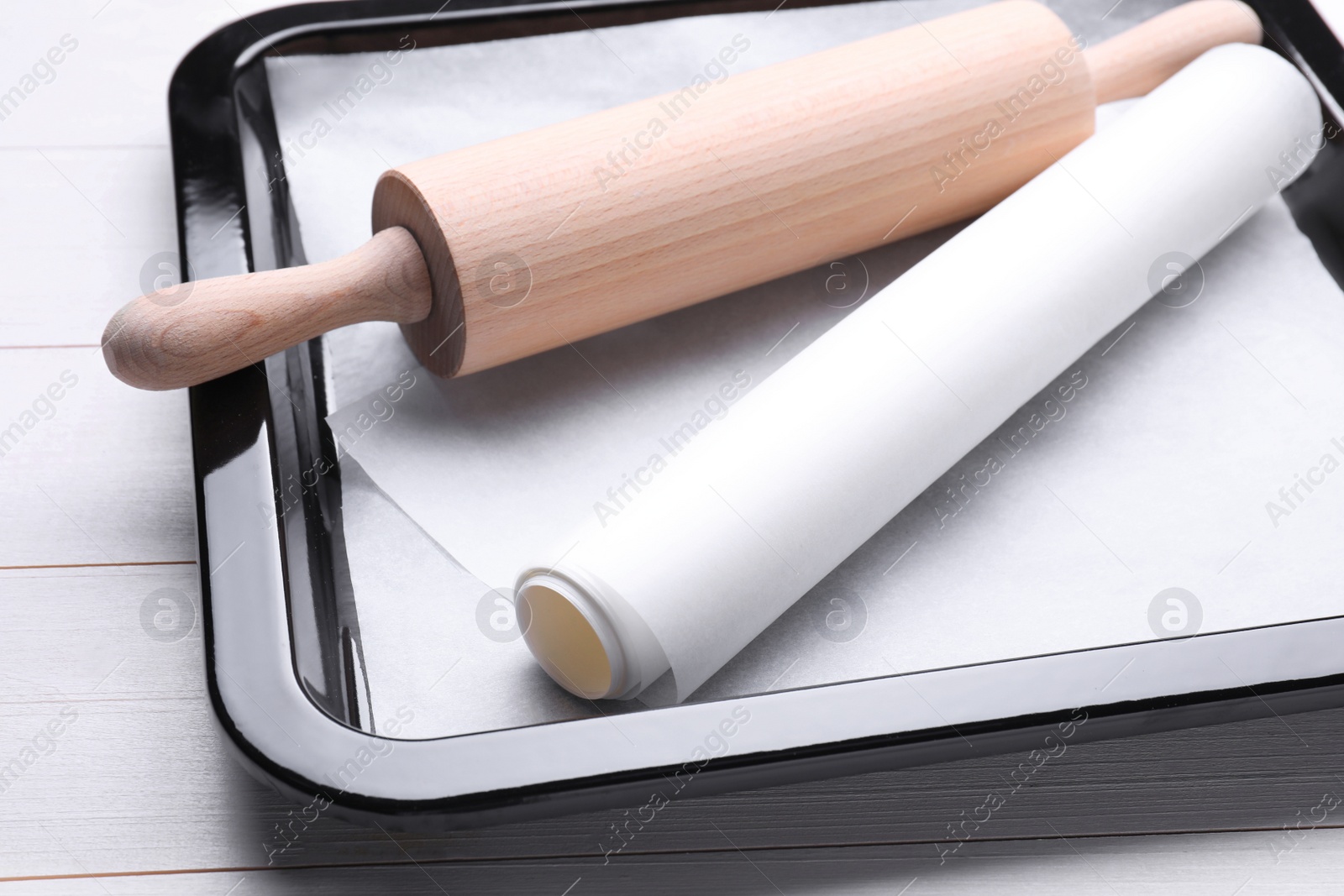 Photo of Baking pan with parchment paper and rolling pin on white wooden table, closeup