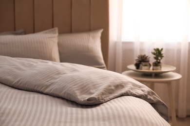 Photo of Comfortable bed with soft blanket near window indoors, closeup