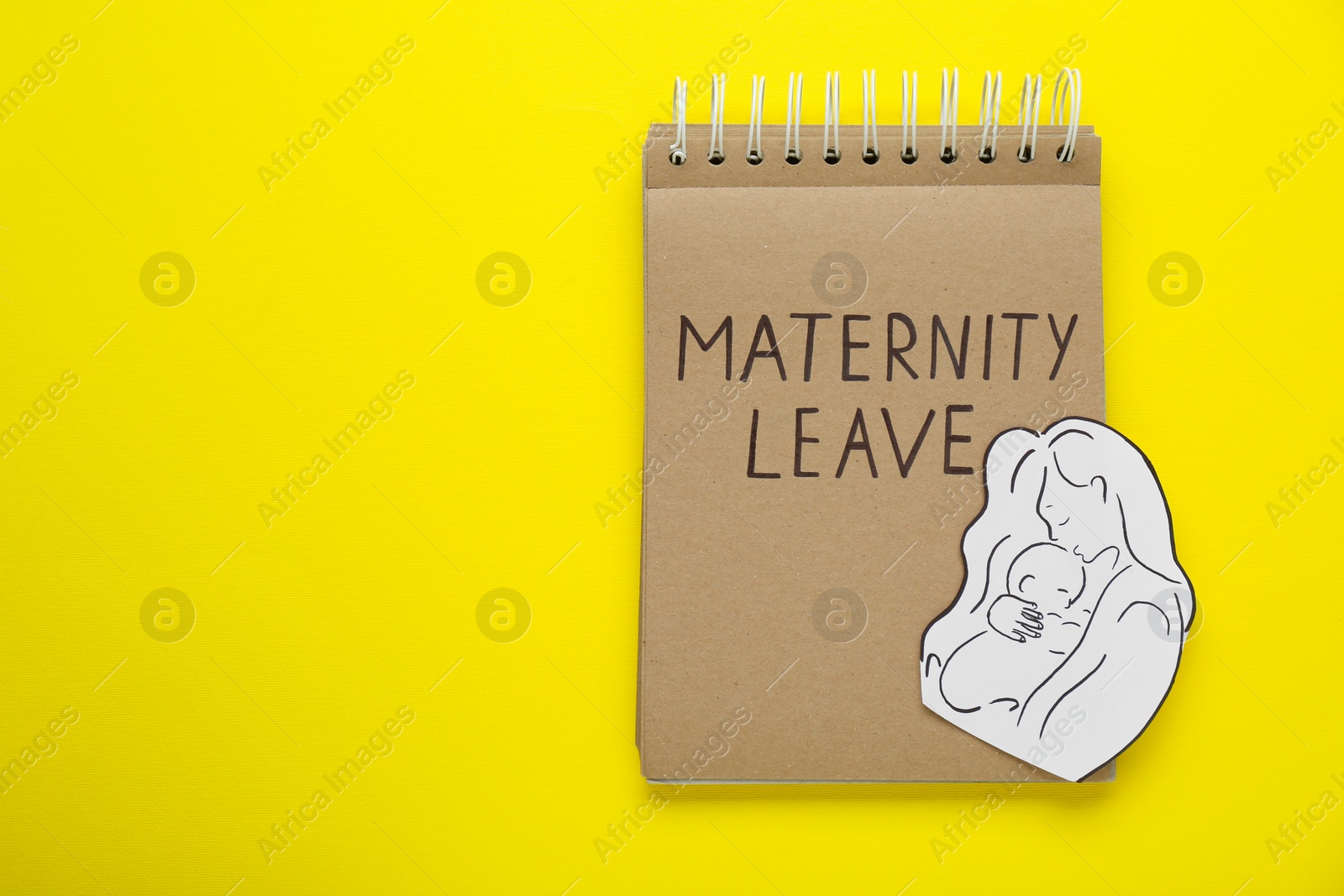 Photo of Maternity leave concept. Notebook with paper cutout of mother and child on yellow background, top view. Space for text