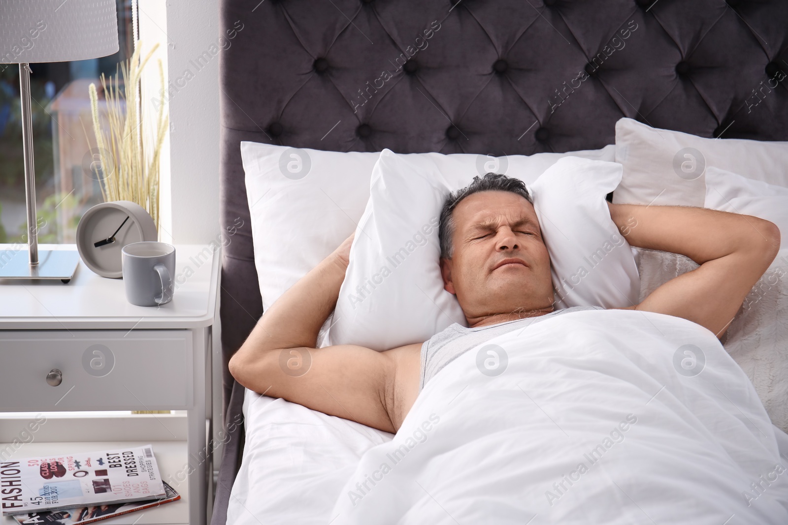 Photo of Man covering ears with pillow while trying to sleep in bed at home