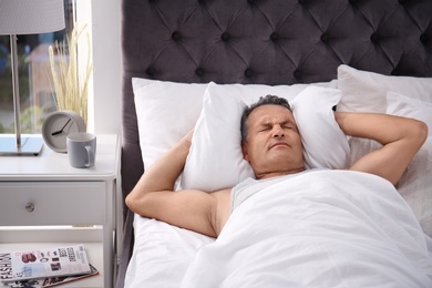 Man covering ears with pillow while trying to sleep in bed at home